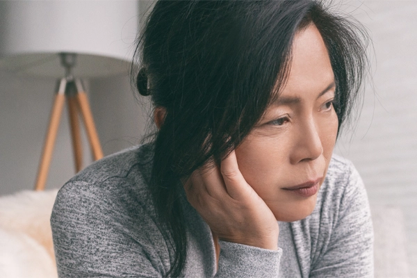 Adrenal-Fatigue-Doctor A middle-aged asian woman sitting on her couch, resting her head on her hand, suffering from adrenal fatigue. Get treatment for adrenal fatigue syndrome from Dr. Stephanie King in Salt Lake City.