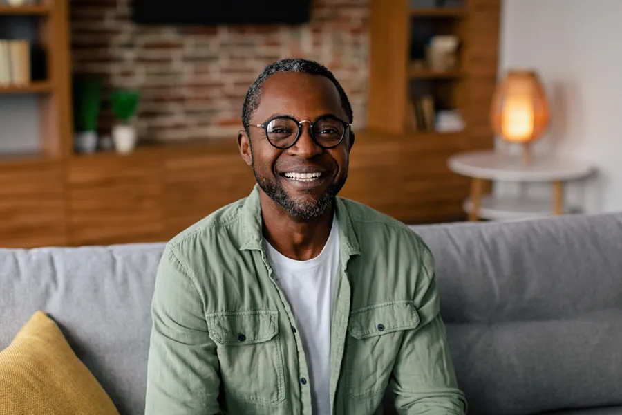 Andropause-Doctor A middle aged black man in a green button up shirt sits on his couch smiling, happy with his treatment for andropause and low testosterone from Dr. Stephanie King in Salt Lake City.