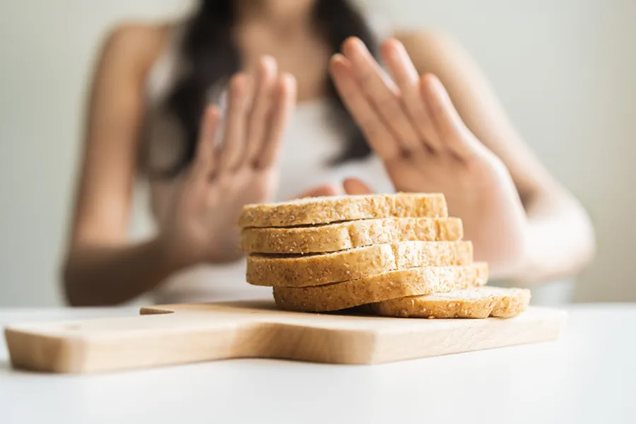 Celiac-Disease-Clinic Close up of a stack of bread slices on a cutting board with a woman's hands behind them, refusing to eat. Get treatment for Celiac Disease from Dr. Stephanie King in Salt Lake City.