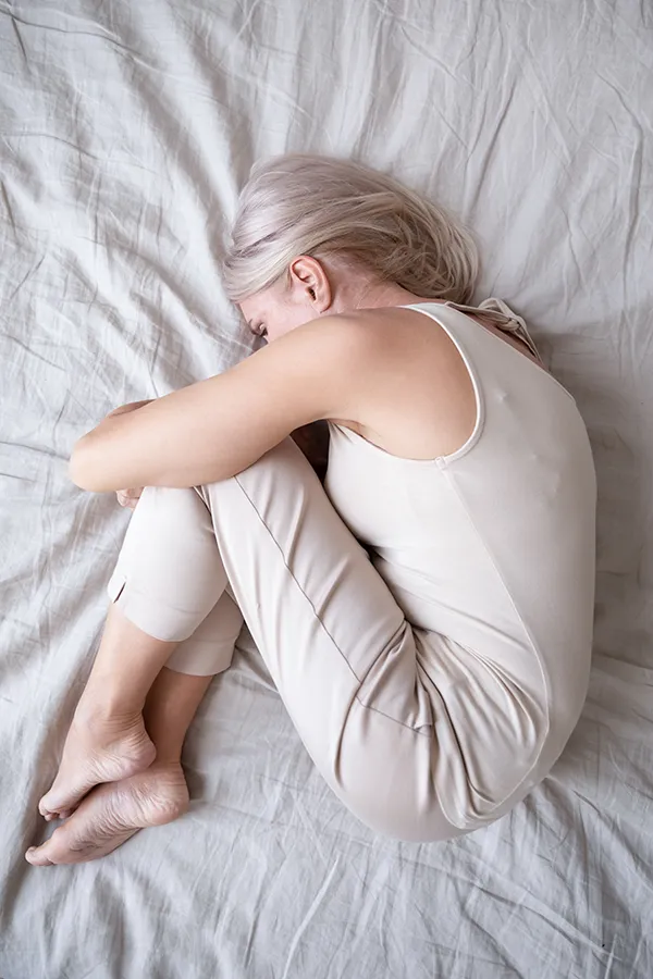 Chronic-Pain-Treatment A woman curled up in the fetal position on her bed. Get chronic pain treatment from Dr. Stephanie King in Salt Lake City.