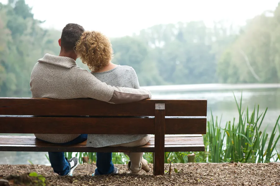 Functional-Medicine-Doctor A couple wearing sweaters seen from behind sitting on a bench and looking out at a relaxing lake and forest, representing functional medicine treatment from Dr. Stephanie King in Salt Lake City.