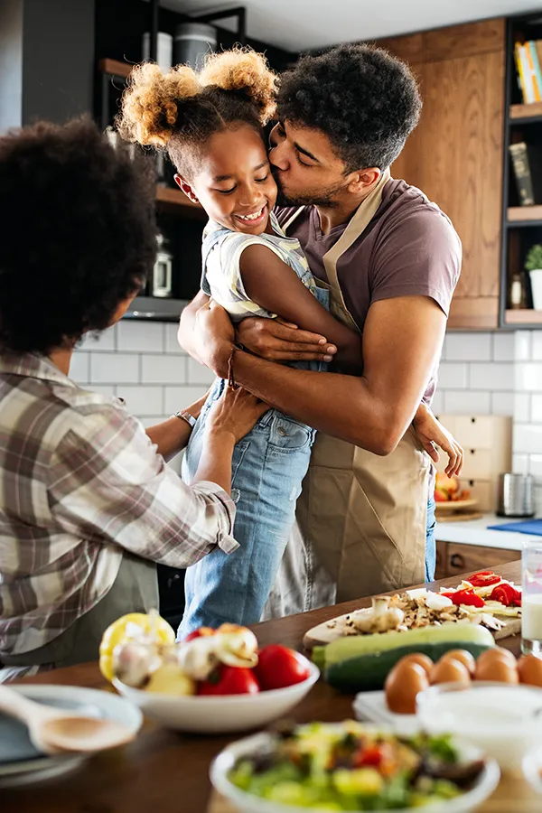 Gut-Health-Treatment A man holds his daughter and kisses her cheek as the family makes a healthy dinner in the kitchen. Get help for digestive issues and gut health from Dr. Stephanie King in Salt Lake City.