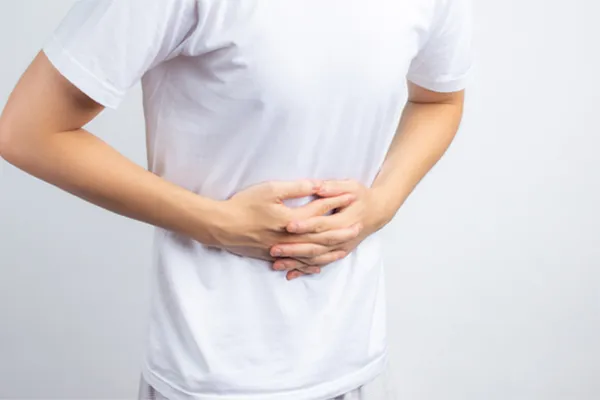Irritable-Bowel-Syndrome-Clinic A person holding their stomach in visible discomfort against a plain background. Dr. Stephanie King treats irritable bowel syndrome with functional medicine in Salt Lake City.