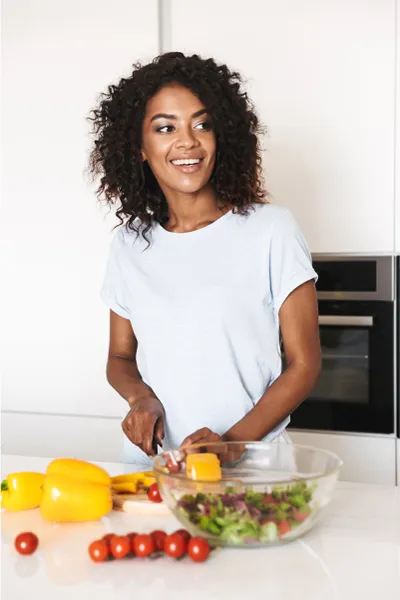 Irritable-Bowel-Syndrome-Treatment Image featuring a smiling woman chopping vegetables for a salad in a bright, white kitchen. Dr. Stephanie King offers Irritable Bowel Syndrome Treatment and Digestive Support in Salt Lake City.