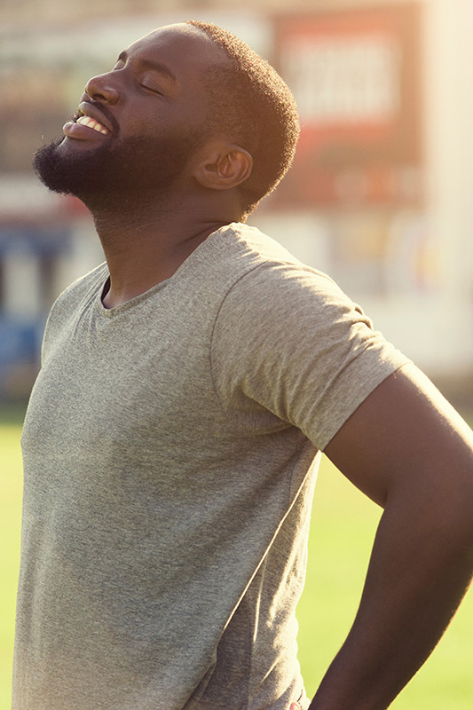 Lean-Muscle-and-Recovery-Treatment A black man in a gray t-shirt and smiles, looking up with closed eyes after a satisfying workout. Get treatment for lean muscle loss and recovery from Dr. Stephanie King in Salt Lake City.