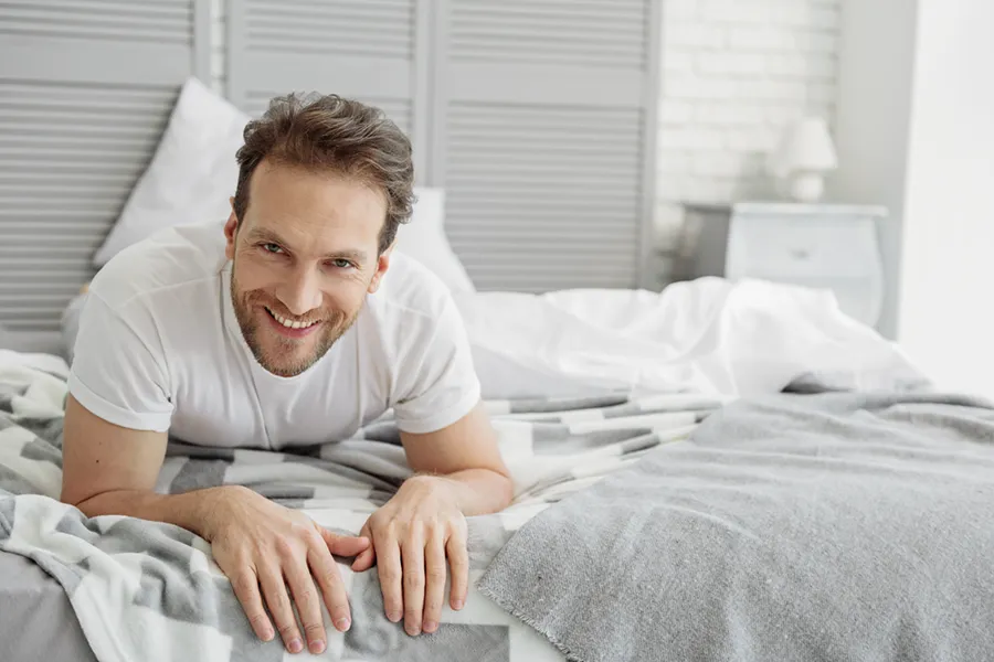 Low-Libido-in-Men-Doctor A dirty-blonde haired man lays on his stomach in bed smiling. Schedule treatment for low libido in men from Dr. Stephanie King in Salt Lake City.