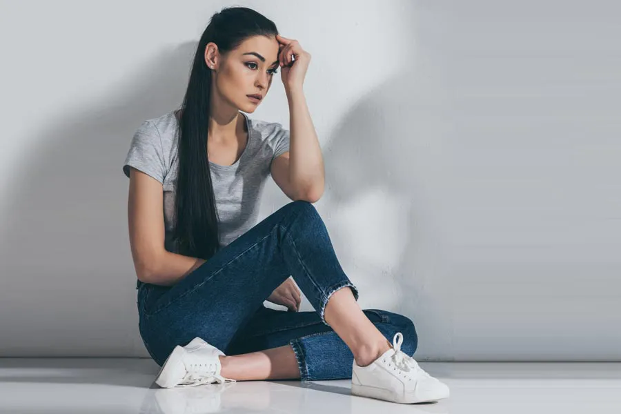 PCOS-Doctor A young brunette woman in a gray t-shirt and jeans sits against a gray wall with her head resting on her hand and a distressed expression. Get help for Polycystic Ovarian Syndrome (PCOS) from Dr. Stephanie King in Salt Lake City.
