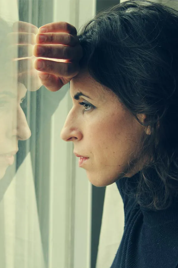 PCOS-Treatment A brunette woman in a thin dark turtleneck looks out the window with a serious expression, suffering from PCOS. Get treatment for Polycistic Ovarian Syndrome/PCOS from Dr. Stephanie King in Salt Lake City.