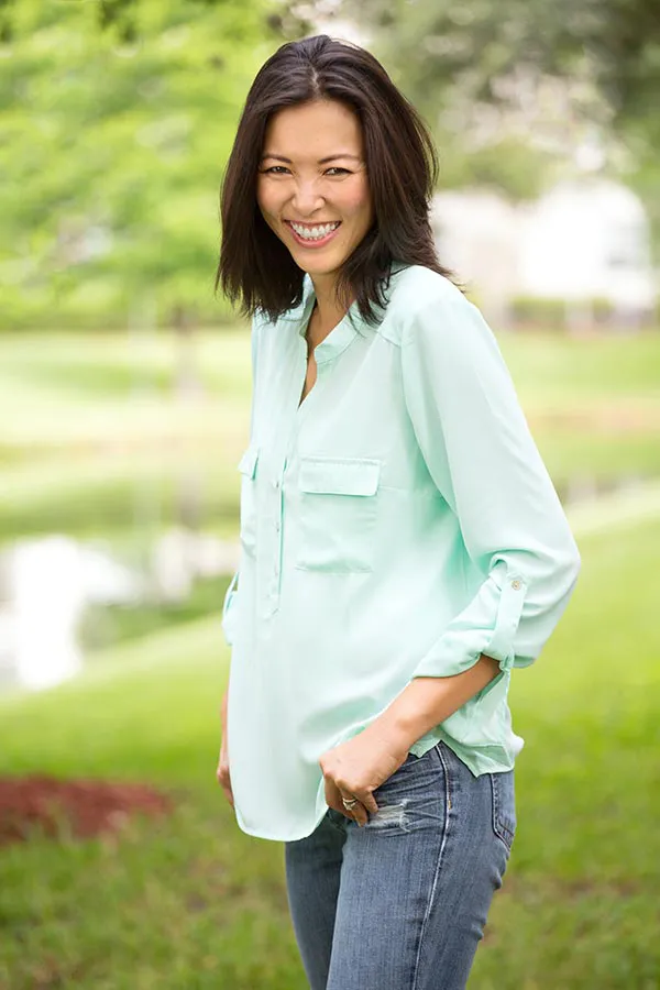 Perimenopause-Treatment A middle-aged brunette woman in a light green button-up shirt stands outside smiling, happy with her perimenopause treatment from Dr. Stephanie King in Salt Lake City.