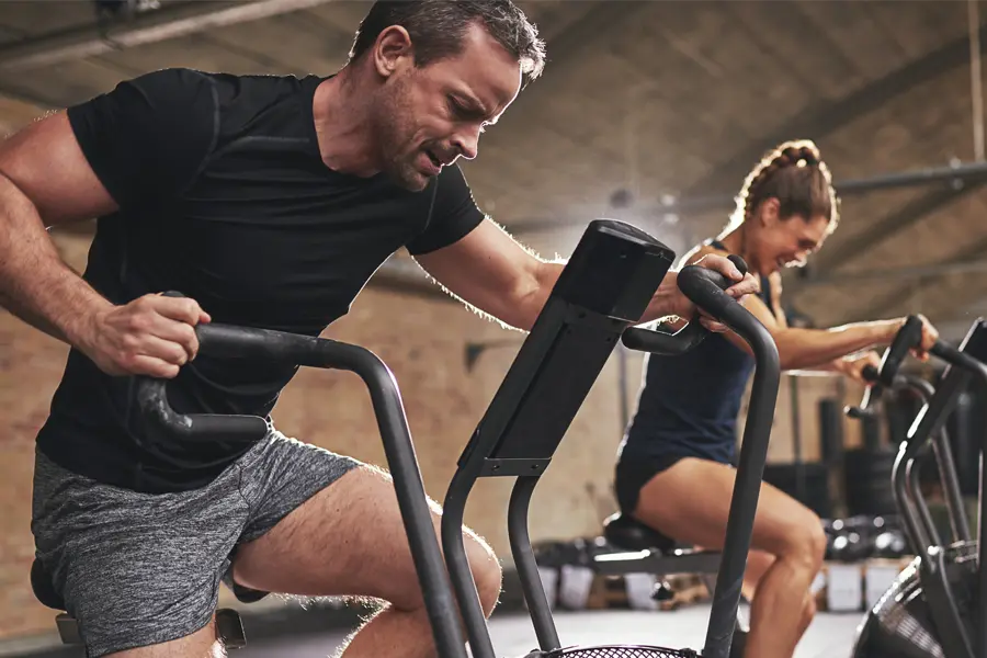 Tirzepatide-Doctor A couple in a brick gym work as hard as they can on exercise bikes, inspired by successful Tirzepatide treatment from Dr. Stephanie King in Salt Lake City.